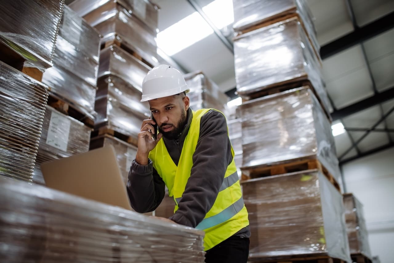 Warehouse worker wearing a helmet and reflective vest managing logistics operations, representing the efficiency and coordination in Del Bravo's supply chain