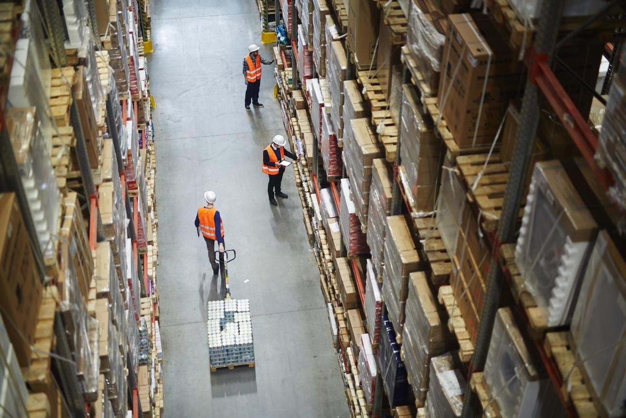 Vista aérea de un almacén con trabajadores revisando mercancías en estantes altos, ilustrando la eficiencia operativa y la gestión precisa de inventarios por parte de Del Bravo