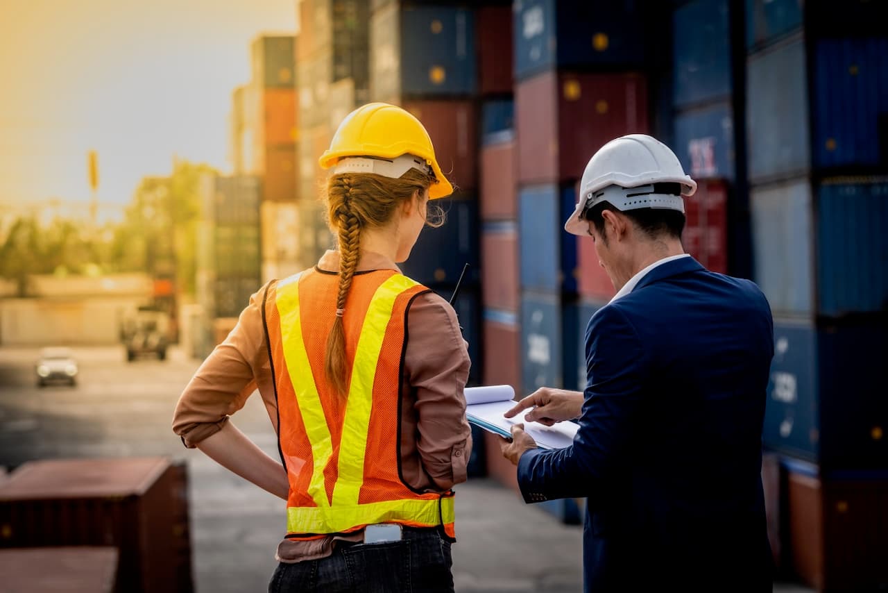 Dos trabajadores revisando documentación en un puerto, reflejando la coordinación y profesionalismo en las operaciones portuarias gestionadas por Del Bravo