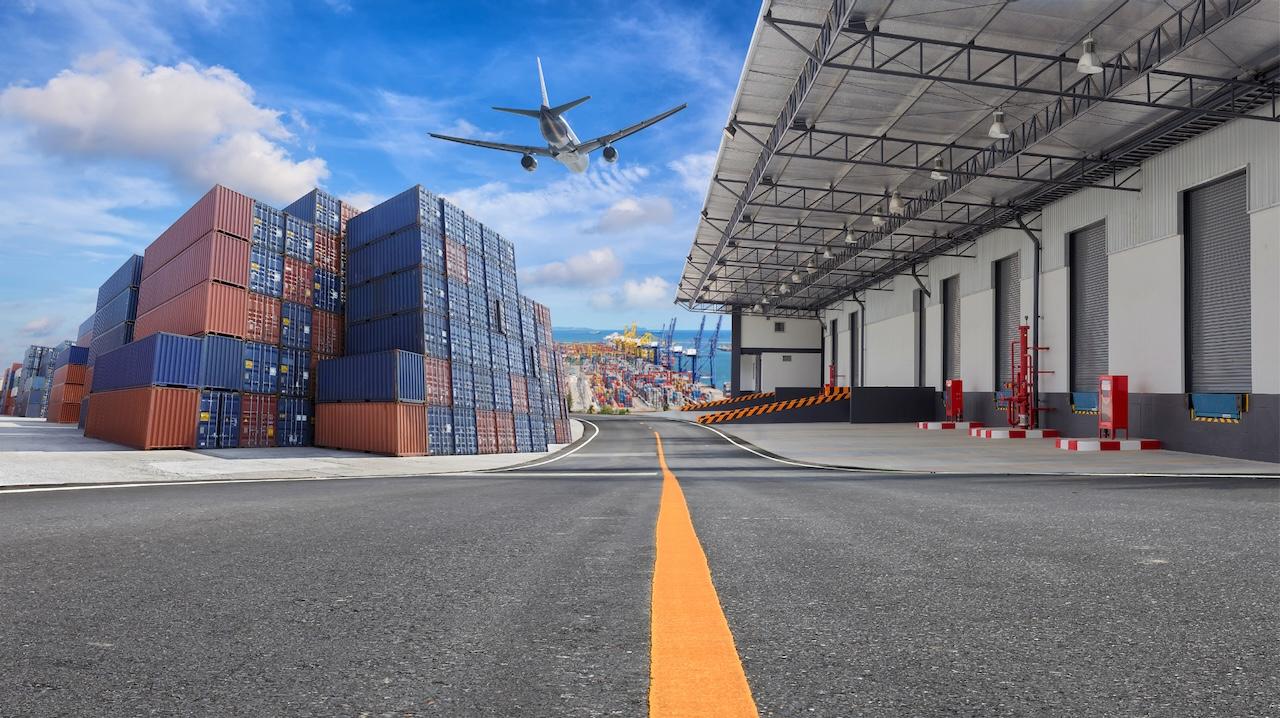 Plane flying over a port with containers and a warehouse, symbolizing Del Bravo's global capacity in air and maritime logistics