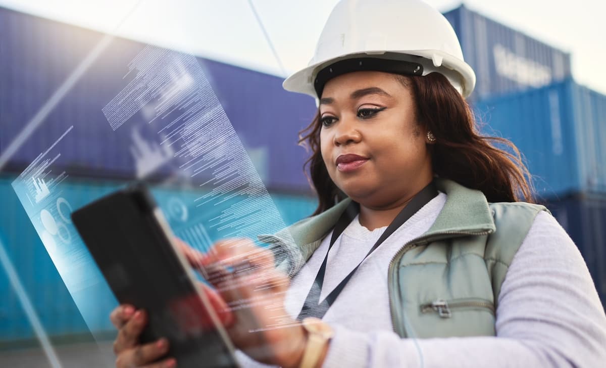 Trabajadora utilizando una tableta digital frente a contenedores en un puerto, destacando el uso de tecnología avanzada en la gestión de operaciones logísticas por parte de Del Bravo