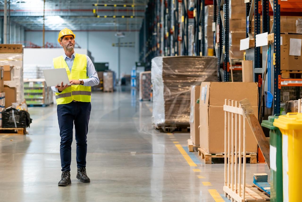 Supervisor wearing a helmet and safety vest reviewing operations in a warehouse, representing efficient control and supervision at Del Bravo's facilities