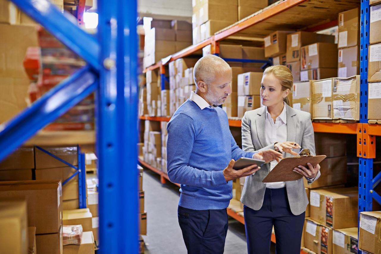 Two professionals collaborating in a warehouse, reviewing documents and using technology, symbolizing coordination and precision in Del Bravo's logistics