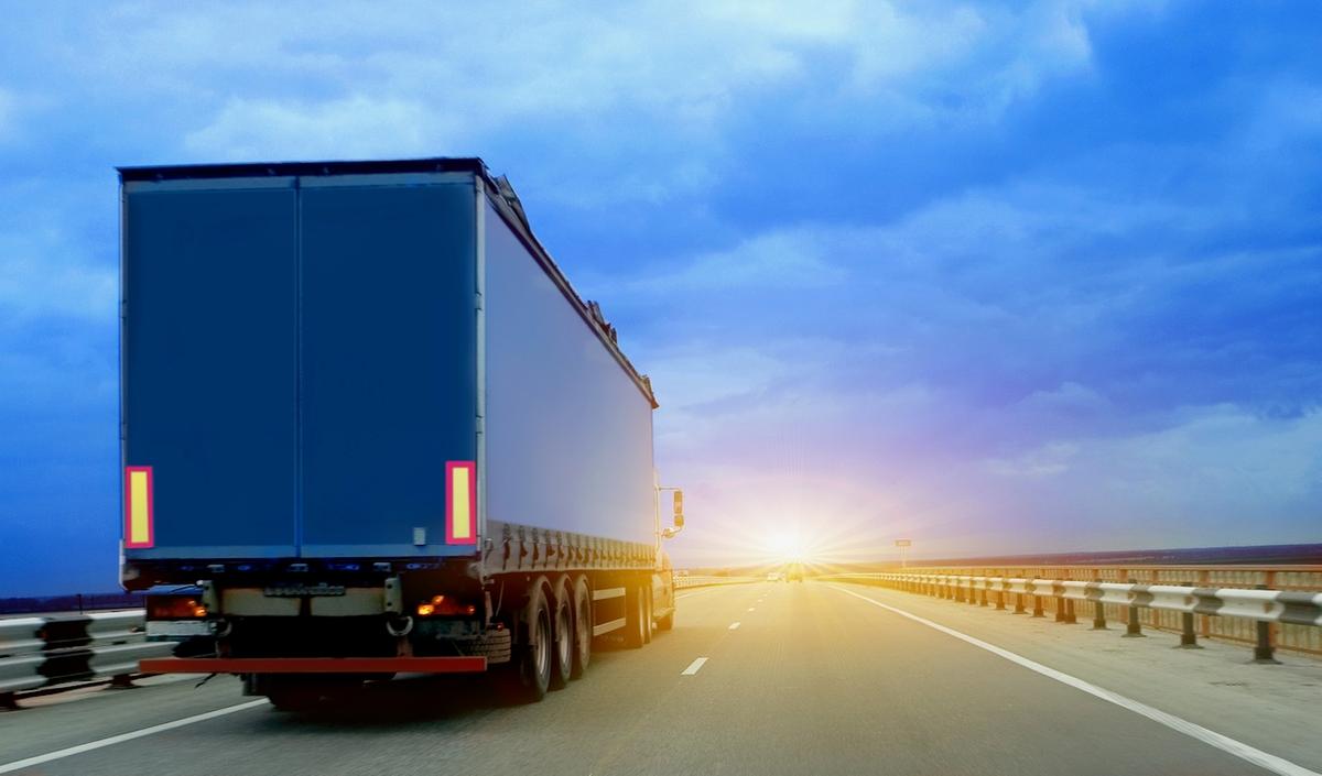 Cargo truck driving on a road at sunrise, symbolizing the reliability and punctuality of ground transportation managed by Del Bravo