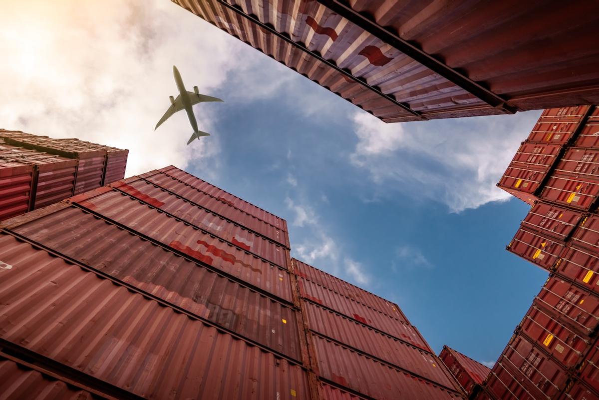 Stacked containers with a plane flying overhead, symbolizing Del Bravo's ability to efficiently handle both air and maritime logistics